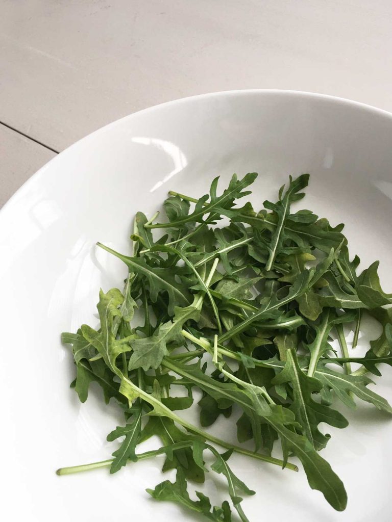 organic baby arugula in a white bowl